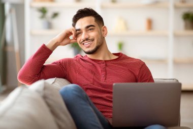 Hayalperest Arap adam evdeki kanepede dinleniyor, dizüstü bilgisayar kullanıyor ve gülümsüyor, internette iş arıyor, kopyalama alanı arıyor. Sevgili bulma sitesinde sörf yapan, kadınlarla sohbet eden mutlu orta doğulu genç adam.