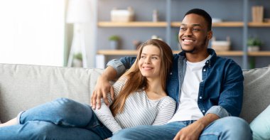 Ev Konforu. Genç Mulikültürel Çifti Sevmek Koltukta Birlikte Rahatlamak, Irklar Arası Romantik Eşler Oturma Odasında Zaman Geçirirken Sarılmak, Haftasonu Eğlencesi, Boşluğu Kopyalamak