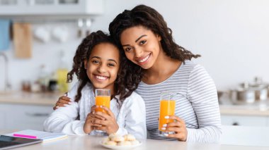Sevimli siyah anne ve kız mutfakta kurabiyelerle portakal suyu içiyor, kameraya bakıyor ve gülümsüyor, fotokopi çekiyor. Mutlu Afro-Amerikan annesi ve çocuğu evde birlikte atıştırıyor.