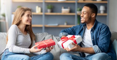 Evde ırklar arası romantik çiftlerin portresi, oturma odasında koltukta oturan ve hediye kutularını saran mutlu çok kültürlü aşıklar, birbirlerini Sevgililer Günü 'yle selamlıyorlar.