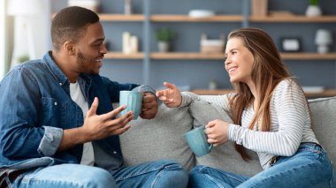 Neşeli, ırklar arası, kahve içip sohbet eden genç, siyah erkek ve beyaz kadın, sıcak içeceklerin ve hoş sohbetlerin keyfini çıkarıyorlar.