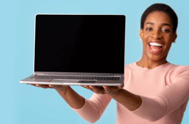 Elinde siyah ekranı olan neşeli Afrikalı Amerikalı kadın, Heyecanlı Kadın Online alışveriş için yeni web sitesi tasarımı yapıyor, Mavi Arkaplan 'da tecrit edilmiş duruyor, Mockup