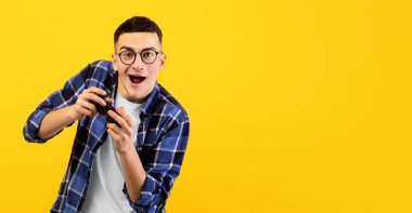 Playstick 'li heyecanlı genç adam turuncu stüdyo arka planında online video oyunu oynuyor. Oyun şampiyonasına ya da yarışmaya katılan denetimci ile neşeli milenyum oyuncusu