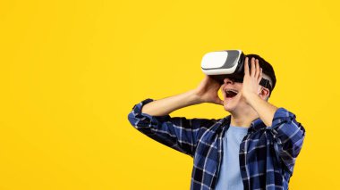 Sanal gerçeklik gözlüklü neşeli genç adam online oyun oynuyor, turuncu stüdyo arka planında heyecanlanıyor. 3D simülasyon, dijital teknolojiler ve modern eğlence konsepti