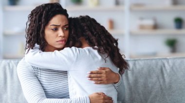 Depresyondaki genç siyah anne kızını kucaklıyor, yakın plan, ev içi, fotokopi odası. Hüsrana uğramış Afrikalı Amerikalı kadın ve kadın çocuğunun ilgiye ihtiyacı var ve anne kucaklamayı seviyor.