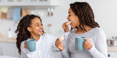 Annesini kurabiyelerle besleyen, mutfakta oturan ve birlikte atıştıran siyah bir kız. Mutlu Afro-Amerikan anne ve kızı evde çay içip, fotokopi çekiyorlar.