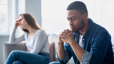 Aile sorunları. Kavgadan sonra koltukta oturan üzgün ırklar arası çiftin portresi, depresyondaki genç çok kültürlü eşler ilişki krizi, seçici odak noktası siyah adam.