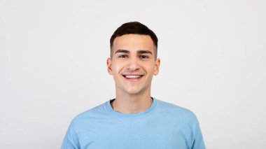 Sıradan giyinmiş yakışıklı beyaz adamın portresi gülümseyen ve açık gri stüdyo arka planından kameraya bakan. Dost canlısı, kaygısız gülüşü olan bin yıllık bir adam.