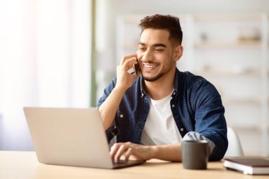 Başarılı bir ortadoğulu adam, evde çalışırken ortaklarıyla cep telefonuyla konuşuyor, akıllı telefon tutuyor ve dizüstü bilgisayara bakıyor, Arap serbest çalışanı iş görüşmesi yapıyor, uzayı kopyalıyor.