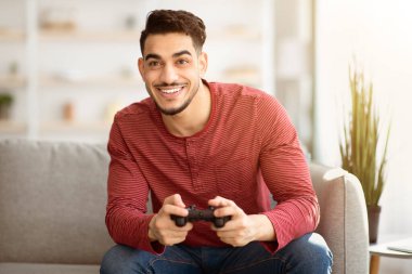 Duygusal ortadoğulu adam evde joystick ile video oyunu oynuyor, fotokopi çekiyor. Mutlu bin yıllar Arap erkeği, hafta sonunun tadını çıkarıyor, oturma odasında kanepede oturuyor, elinde joystick, kumar oynuyor.