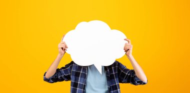 Portakal rengi stüdyo arka planında boş konuşma balonu tutan tanınmamış genç adam tasarım için maket yapıyor. Boş kelime bulutu olan milenyum adamı, reklamın için yer.