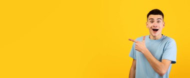 Heyecanlı genç adam şok içinde ağzını açıyor ve turuncu stüdyo arka planındaki boş alanı işaret ediyor, afiş tasarımı. Hayret bir şey, milenyum adamı reklam ürünü, büyük indirim teklif ediyor.