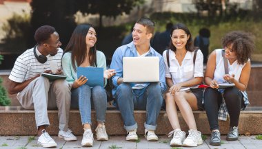 Kampüste dizüstü bilgisayarla oturup birlikte gülen neşeli üniversite öğrencileri, derslere ara verip, panorama