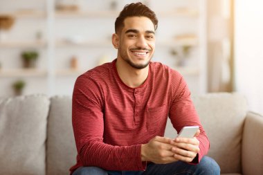 Olumlu Arap adam evde yepyeni bir cep telefonu kullanıyor arkadaşlarıyla online parti veriyor telekomünikasyon için güzel bir mobil uygulama kullanıyor. Akıllı telefon tutan mutlu orta doğulu adam, kopyala uzay