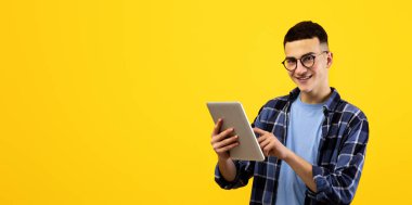 Çevrimiçi yaşam konsepti. Turuncu stüdyo arka planında tablet kullanan genç bir adam. Dokunmatik Sörf Ağı olan neşeli milenyum çocuğu, video izliyor, e-postaları kontrol ediyor, sosyal medyada paylaşıyor.