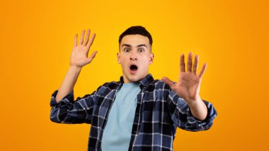 Korkak beyaz adam panik içinde bağırıyor, iki eli turuncu stüdyo arka planında duraksama hareketi yapıyor. Korkmuş milenyum adamı kendini korumaya çalışıyor, yeterince el kol hareketi yapıyor.