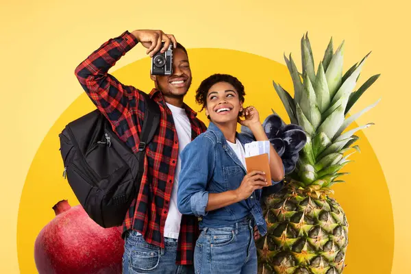 Afrikalı Amerikalı çift renkli bir meyve kolajının önünde neşeli poz veriyor, tatile çıkıyorlar.