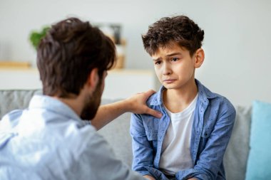 Baba ve üzgün oğul evde kalp kalbe konuşuyorlar, baba sorunları çözmeye çalışıyor, birlikte çözüm arıyorlar. Ebeveyn sevgi ve özen gösteriyor, çocuğu sakinleştiriyor ve omuz omuza tutuşuyor.