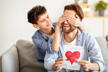 Babalar Günü 'nde babasına sürpriz yapan mutlu bir oğul. Gözlerini arkadan kapatıyor, evde kanepede oturan babasıyla el yapımı tebrik kartı veriyor. Aile bayramı kutlaması