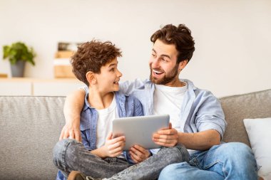 Aile hafta sonu. Baba ve oğlunu tablet bilgisayar kullanarak tüketti, evde birlikte vakit geçirirken internette sörf yaptı oturma odasında kanepede oturdu, fotokopi çekti. Modern teknoloji kavramı