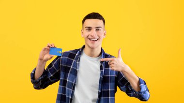 Portakal rengi stüdyo arka planında kredi kartını gösteren mutlu milenyum çocuğu portresi. Tatmin olmuş banka müşterisi, temassız ödemeyi teşvik ediyor, elektronik para hizmetleri öneriyor