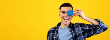 Portakal rengi stüdyo geçmişi üzerinden gözünü kredi kartıyla kapatan yakışıklı bir genç. Pozitif banka müşterisi finansal hizmetler öneriyor, elektronik para kullanıyor, bağlantısız ödeme yapıyor.