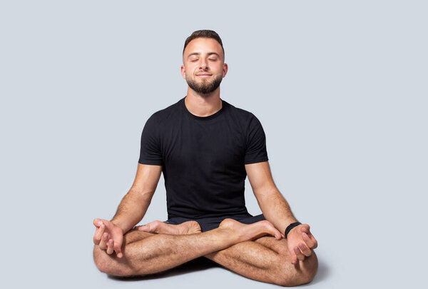 Positive millennial european man with beard in sportswear practice yoga in lotus position, enjoy breath exercises, calm, peace and health care, isolated on gray studio background