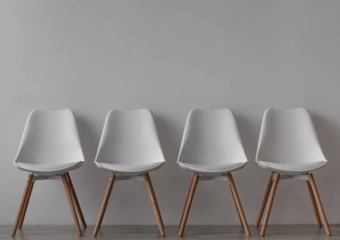 Ofiste ya da oturma odasında gri duvar arkasında dört boş beyaz sandalye. Basit iç mimari, minimalist tasarım. Kriz ve kendini izole etme, covid-19 salgını, reklam ve satış, kapalı alan, kopyalama alanı, modelleme