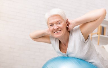 Mutlu aktif Olgun kadın fitness topu evde, boş alan ile yapıyor