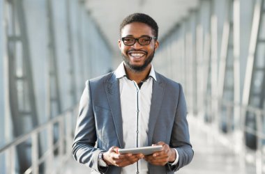 Afro-Amerikalı İşadamı, Dijital Tablet kullanarak Havalimanı 'nda yürürken kameraya gülümsüyor. İş Seyahat Uygulaması Kavramı.