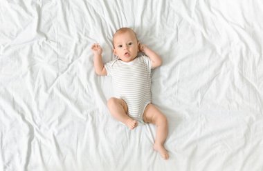 Yatakta uzanmış bebek kıyafetleri içinde, kameraya merakla bakan bebek manzarası.
