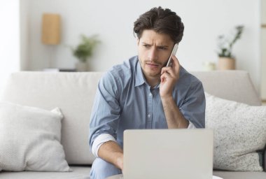 Ciddi Guy Evde Kanepede Oturan Laptop Üzerinde Çalışan Tatsız Telefon Görüşmesi Having. Boş Alan