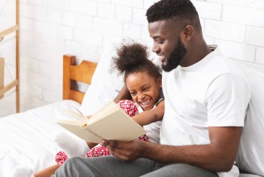 Hikaye zamanı. Afrikalı amerikalı baba yı seviyorum küçük kızına peri masalları okuyor, yatakta birlikte oturuyor.