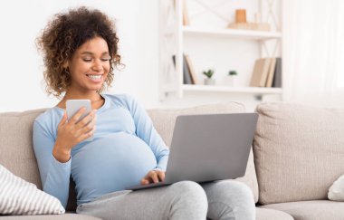 Teknoloji aletleri, dizüstü bilgisayar ve cep telefonu kullanan mutlu bir kadın. Kanepede dinleniyor.