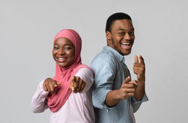 Biz seni seçiyoruz. Neşeli siyahi aşıklar kameraya bakıyor, gri stüdyo arka planında neşeli pozlar veriyor. Mutlu Afro-Amerikan erkek ve kadın tesettürde kameraya bakıyor.