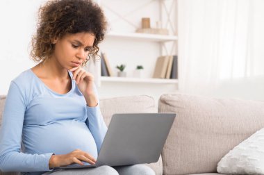 Karmaşık afro beklenen kadın dizüstü bilgisayar kullanıyor, yeni doğan bebek için bir şeyler alıyor, boş yer var.