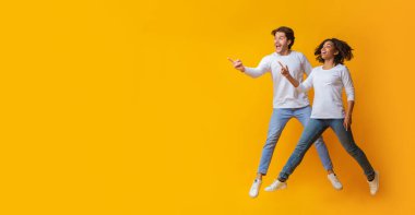 Harika bir tanıtım. Havaya sıçrayan ve sarı arka plandaki kopyalama alanına bakan ırklar arası bir çift.