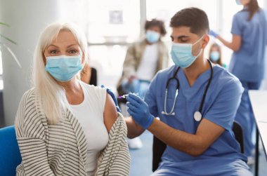 Covid-19 Aşılama. Kıdemli hasta kadın Coronavirus aşısı oluyor. Hastanede doktorla oturuyor, maske takıyor. Doktor Corona Virüs Aşısını Yaşlı Kadın 'a Enjekte Ediyor
