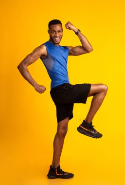 Workout Concept. Energetic afro man doing high knees exercise, lifting leg and waving hands, free space, full length