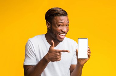 Sarı arka planda duran kameraya gülümseyen, elinde boş ekranla akıllı telefonu işaret eden Afro Adam. Model