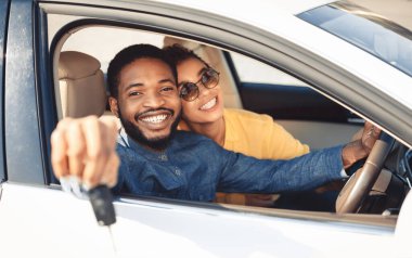 Kendi otomobili. Afrika kökenli Amerikalı eşler otomobilde oturan kameraya yeni araba anahtarı gösteriyor. Seçici Odaklanma