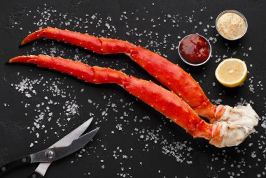 Gurme deniz ürünleri. Araçlar ve soslar siyah tuzlu masaya, üstten görünüm yeme ile pişmiş Kral Yengeç bacakları hizmet