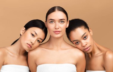 Vücut Bakımı. Havluya sarılı üç farklı kız model bej arka plandaki kameraya bakıyor. Stüdyo Çekimi