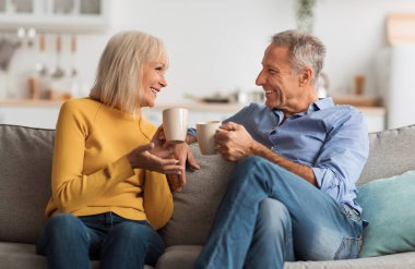 Neşeli, olgun bir çift çay içiyor ve evdeki koltukta oturup konuşuyor. Emekli kıdemli eşler ellerinde kahve bardaklarıyla hafta sonu sohbetinin tadını çıkarıyorlar. Emeklilik Yaşam Tarzı, Mutlu Evlilikler