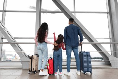 Hava Yolculuğu. Kızı havaalanında uçaktan ayrılan bir kıza bakan aile, küçük bir kız çocuğu, Terminalde elinde bavullarla bekleyen genç ebeveynlerin ve kız çocuğunun arka plan görüntüsü.