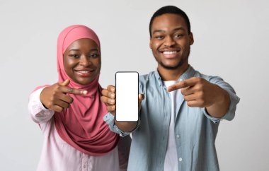 Neşeli, siyah, yakışıklı bir çift ve tesettürlü genç bir bayan boş ekranla akıllı telefona bakıyor. Mutlu Afro-Amerikan Müslüman ailesi cep telefonuna uygulama öneriyor.