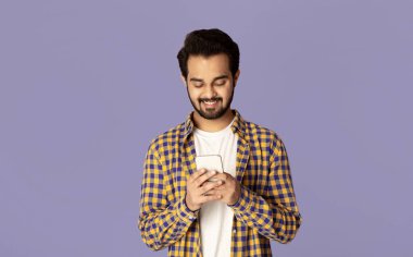 Pozitif Hintli adam cep telefonu ekranına bakıyor ve menekşe arkaplanda gülümsüyor.