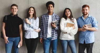 Eğitim kavramı. Öğrenciler gri duvar üzerinden kameraya gülümsüyor, üniversitede mola