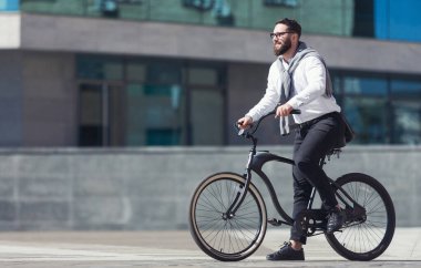 Neşeli, aktif, gözlüklü iş adamı bisiklet sürüp boş alana gidiyor.