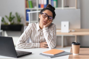 Modern ofis içinde dizüstü bilgisayarda çalışırken iş yerinde uyuyan yorgun bir iş kadını. Uykusuzluk ve yorgunluk sorunu, sıkıcı iş kavramı